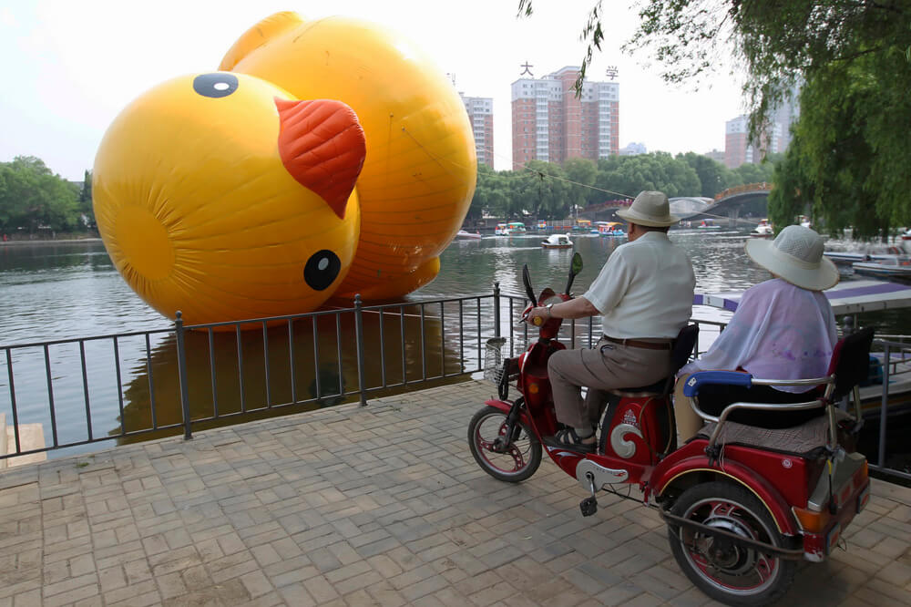 Visitors look at a scaled replica of the rubber duck by Dutch conceptual artist Florentijn Hofman as employees try to pull it upright on a lake at a park in Shenyang