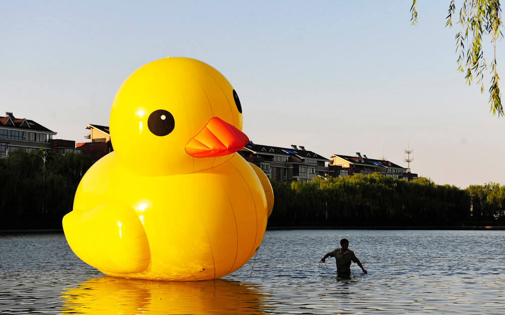 A labourer walks in water after setting up a scaled replica of the rubber duck, by Dutch conceptual artist Hofman, on an artificial lake in Luoyang